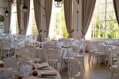 Miniature Réception à l'Orangerie Salon lumineux avec fauteuils bleus, table basse, cheminée, lampes, cadres au mur et grande fenêtre avec rideaux fleuris.
