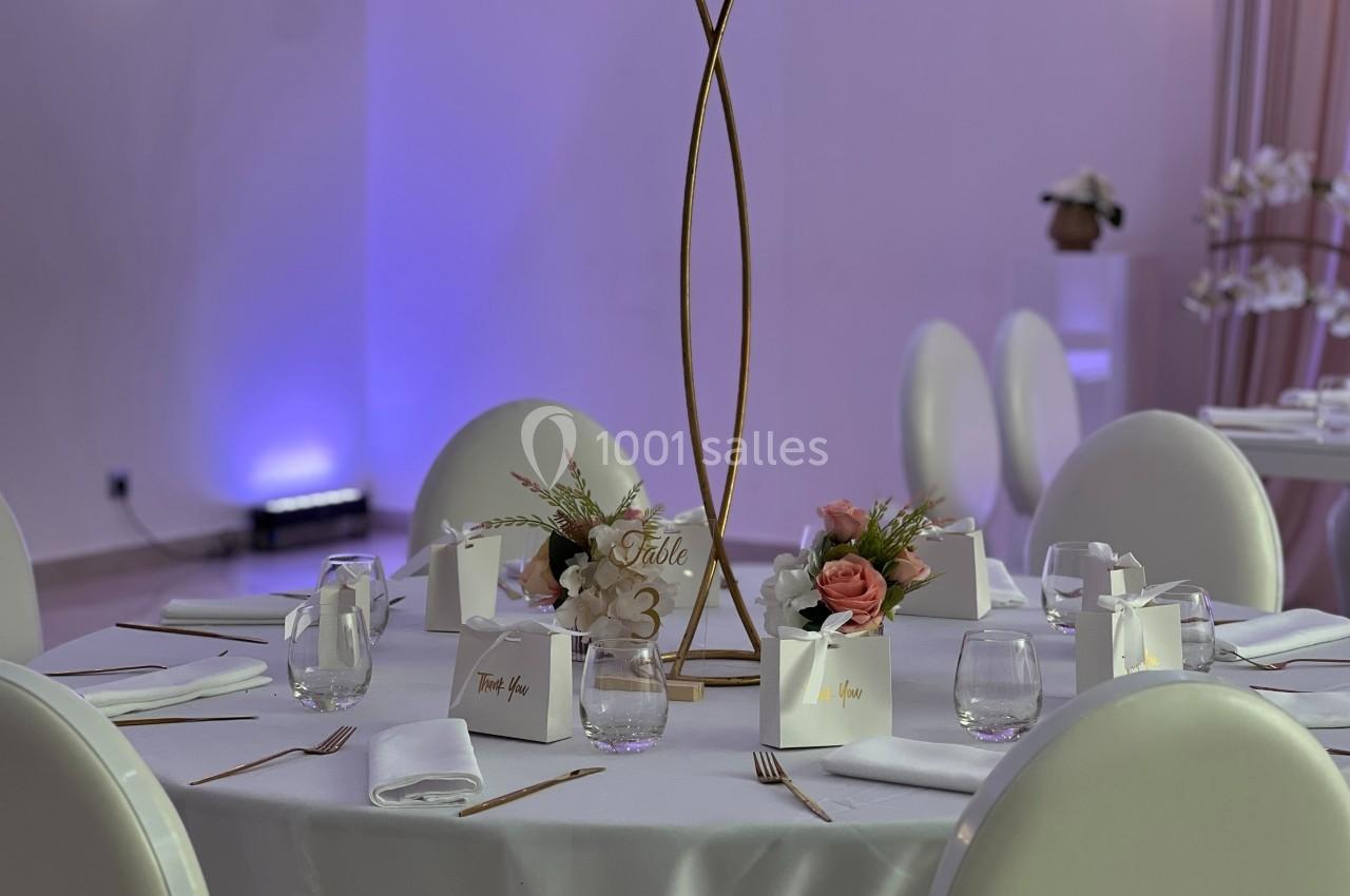 Table élégamment dressée avec des chaises blanches, décorations florales et marque-places dans une ambiance lumineuse.