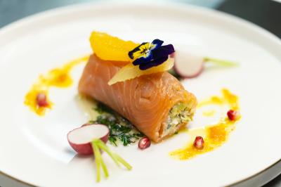 Rouleau croustillant servi sur un lit de légumes colorés avec une garniture florale sur une assiette blanche.