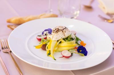 Rouleau croustillant servi sur un lit de légumes colorés avec une garniture florale sur une assiette blanche.
