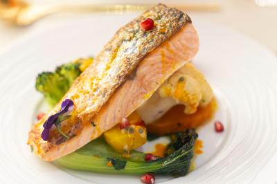 Rouleau croustillant servi sur un lit de légumes colorés avec une garniture florale sur une assiette blanche.