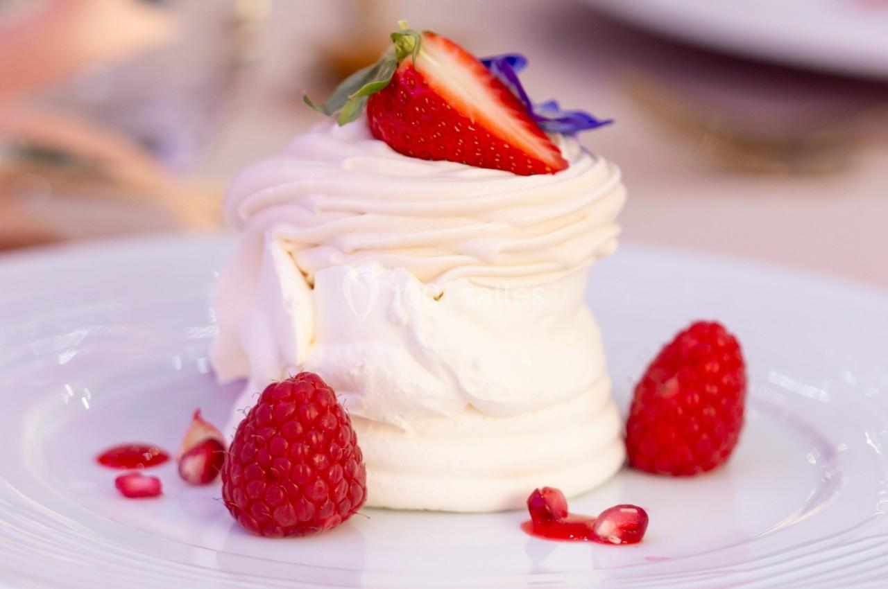 Dessert meringué garni de crème, fraise, framboises et pétales comestibles, présenté sur une assiette blanche.