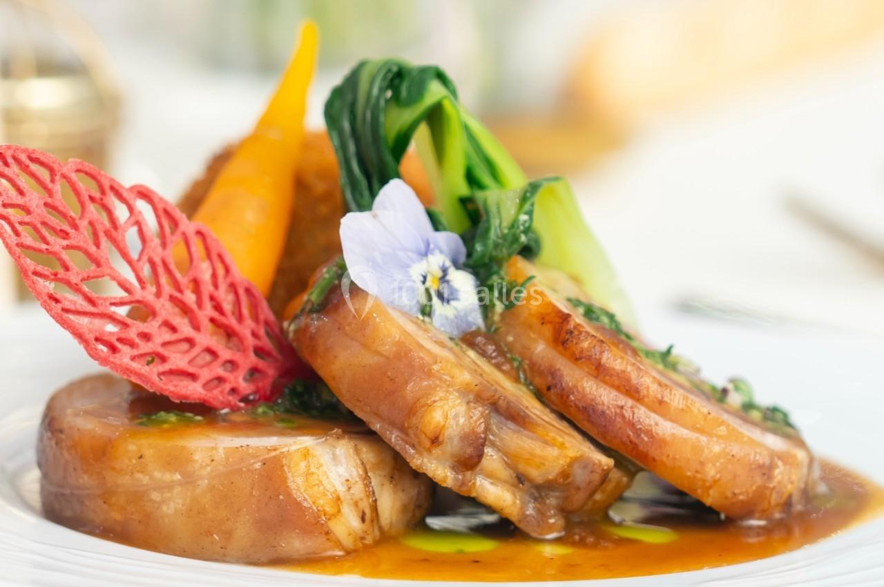 Plat gastronomique composé de viande, légumes colorés, sauce et décorations comestibles sur une assiette blanche.