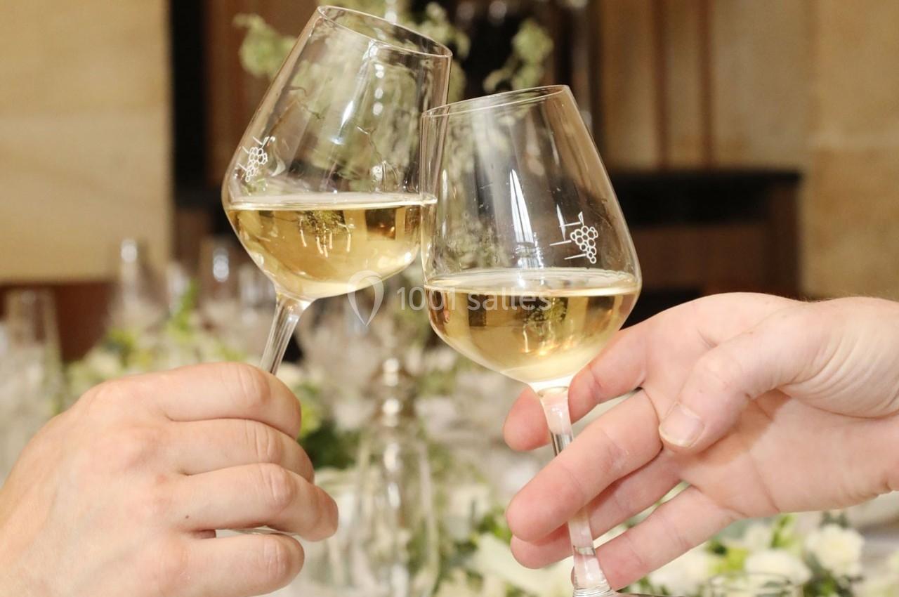 Deux verres de vin blanc portés pour un toast, avec une table décorée en arrière-plan flou.