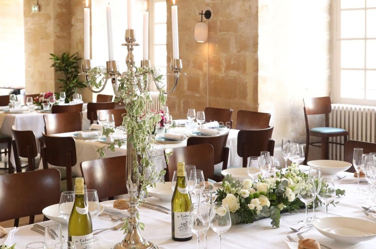 Salle de réception élégante avec tables dressées, chandeliers, fleurs blanches et bouteilles de vin.