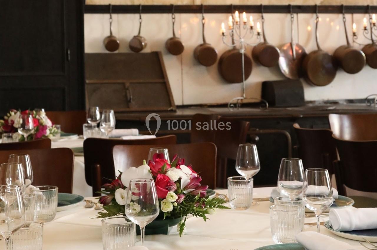 Salle à manger élégante avec tables dressées, compositions florales et cuisine ancienne en arrière-plan.