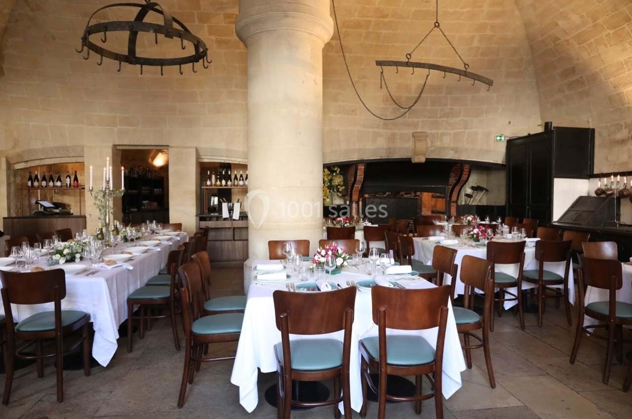 Salle de restaurant avec tables dressées, nappes blanches, chaises en bois et décor en pierre voûtée.