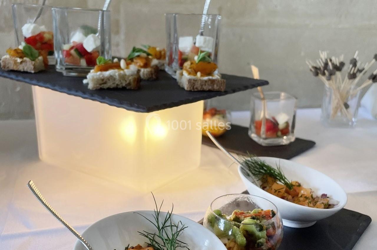 Plateau de verrines et bouchées apéritives variées disposées sur une table blanche avec éclairage décoratif.