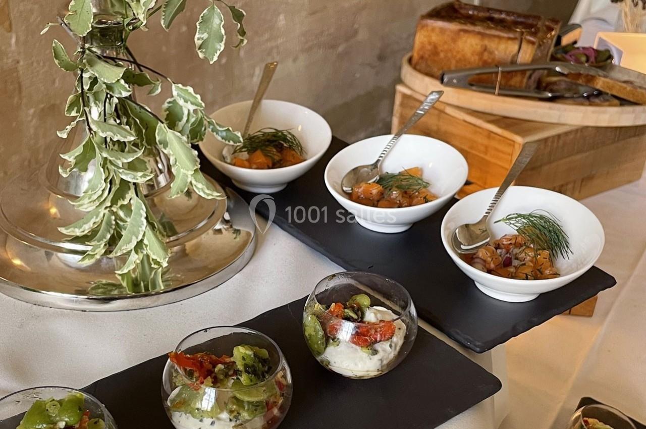 Assortiment de verrines et bols garnis de préparations culinaires, disposés sur une table décorée de feuillage.