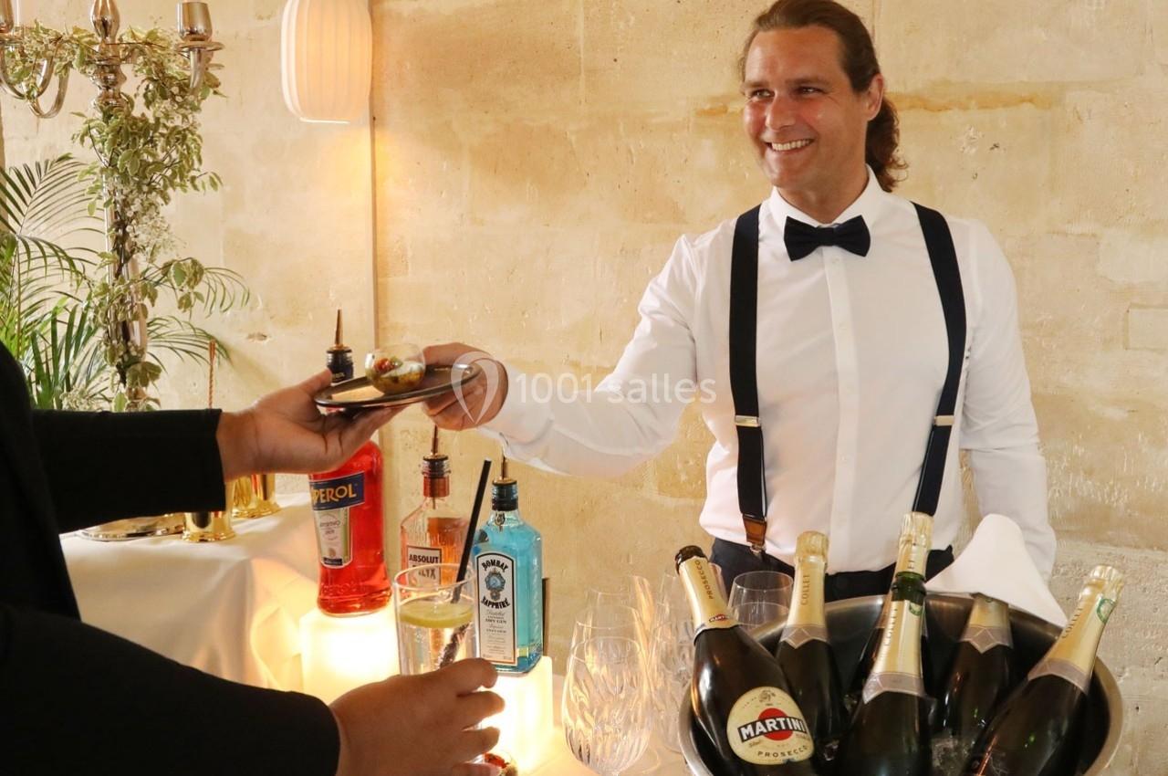 Un serveur souriant en chemise blanche et nœud papillon sert un amuse-bouche lors d'une réception avec boissons.