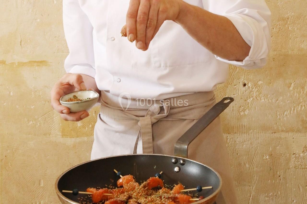 Un chef saupoudre des graines sur des brochettes de saumon dans une poêle.