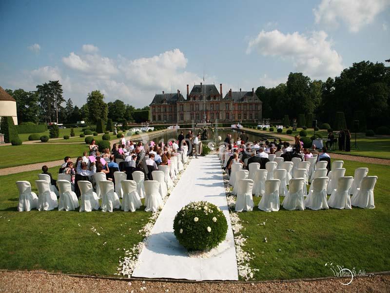 Cérémonie de mariage en plein air avec des invités assis face à un château entouré de jardins.