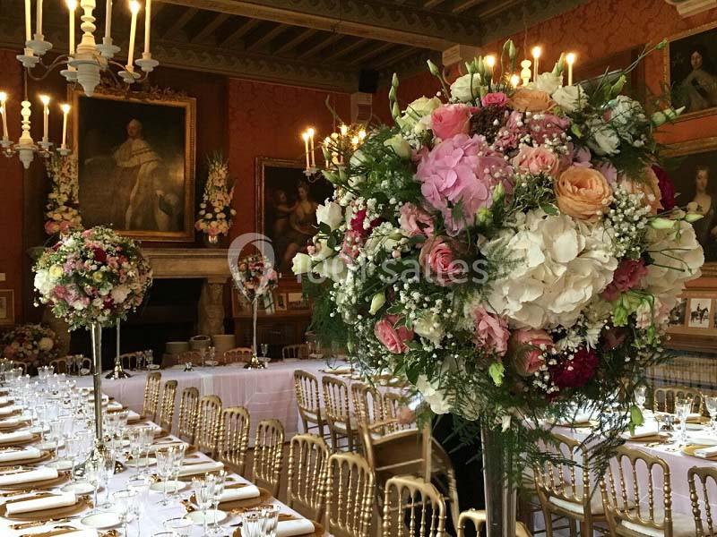 Salle de réception élégante décorée avec des chandeliers, des tables dressées et de grands bouquets de fleurs colorées.