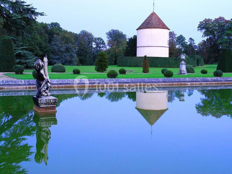 Étang reflétant un pigeonnier rond, entouré de pelouse, d'arbres et de statues dans un jardin paysager.