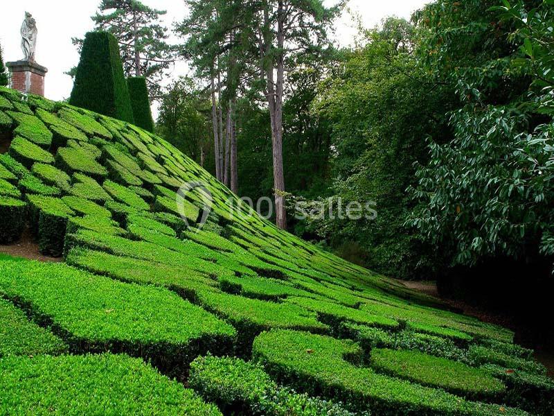 Haie taillée en formes géométriques sur une pente, entourée d'arbres et surmontée d'une statue.