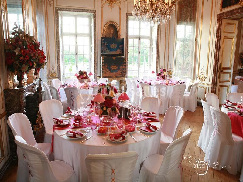 Salle élégante avec tables rondes dressées, nappes blanches, décorations florales et lumière naturelle entrant par de…