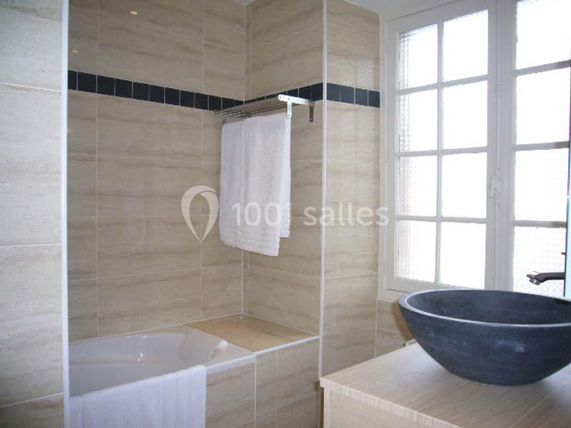 Salle de bain avec baignoire encastrée, serviette suspendue, vasque noire sur meuble en bois et fenêtre vitrée.