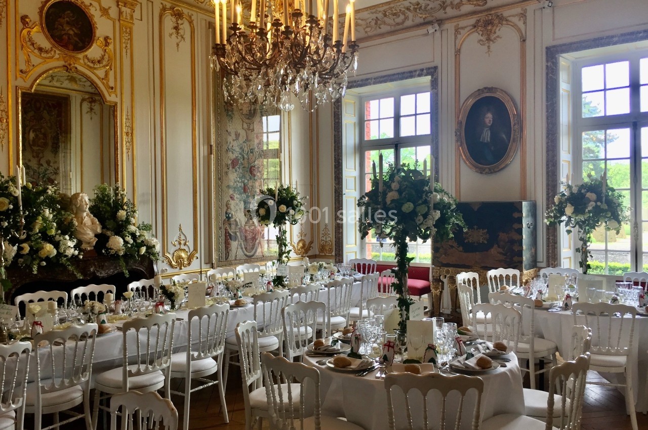 Salle de réception élégante avec tables dressées, décorations florales et lustre en cristal dans un cadre classique.