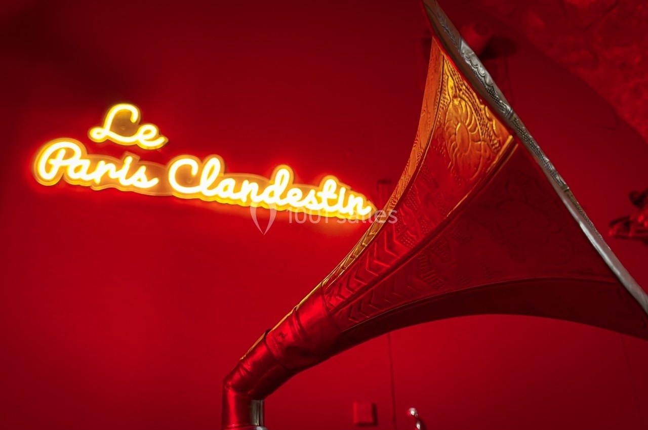 Enseigne lumineuse ’Le Paris Clandestin’ sur un mur rouge, avec un gramophone ancien en premier plan.