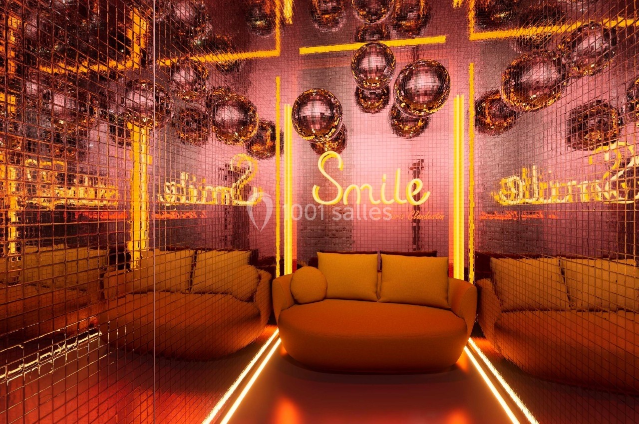 Salle aux murs recouverts de miroirs dorés, canapé orange et enseigne lumineuse ’Smile’ entourée de boules disco.