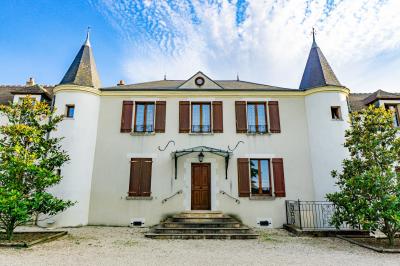 Champ de coquelicots rouges au premier plan avec un bâtiment en pierre et des toits en arrière-plan sous un ciel nuageux.