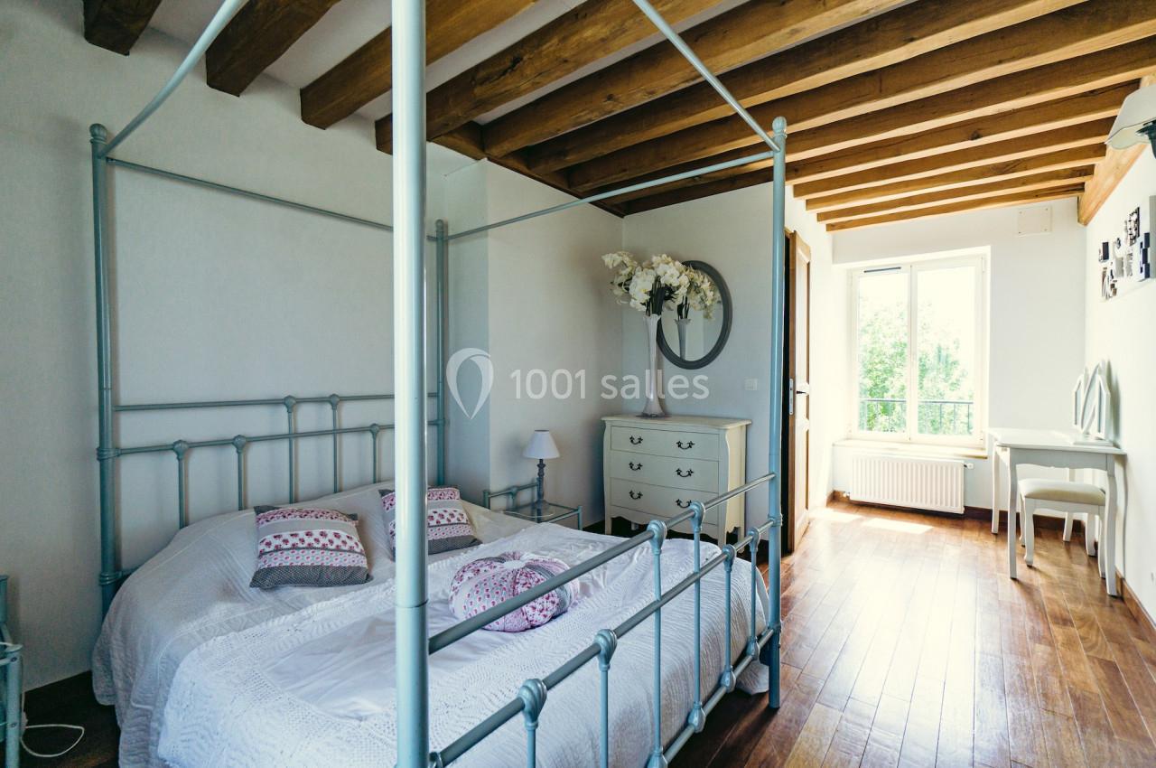 Chambre lumineuse avec lit à baldaquin, plafond en poutres apparentes, parquet en bois et fenêtre donnant sur un jardin.