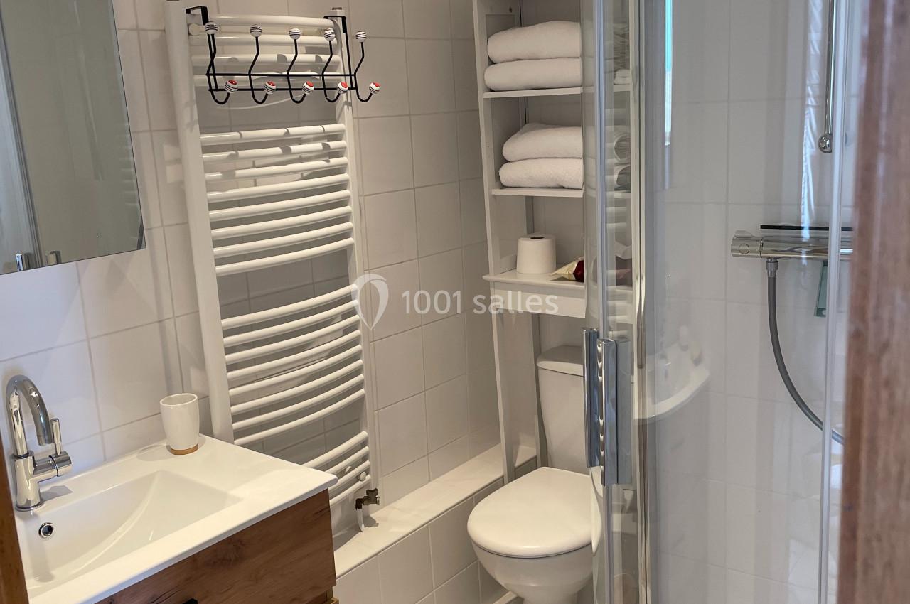 Salle de bain moderne avec douche arrondie, lavabo avec meuble en bois, toilettes et étagères avec serviettes.