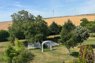 Champ de coquelicots rouges au premier plan avec un bâtiment en pierre et des toits en arrière-plan sous un ciel nuageux.