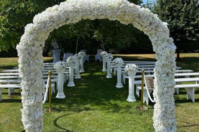 Champ de coquelicots rouges au premier plan avec un bâtiment en pierre et des toits en arrière-plan sous un ciel nuageux.