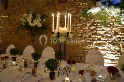 Cour éclairée au crépuscule avec des bâtiments en pierre, des torches allumées et des personnes en arrière-plan.