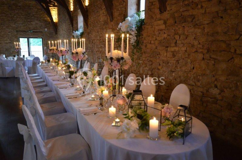 Grande table de réception décorée avec chandeliers, fleurs et bougies, dans une salle aux murs en pierre apparente.