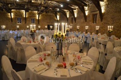 Cour éclairée au crépuscule avec des bâtiments en pierre, des torches allumées et des personnes en arrière-plan.