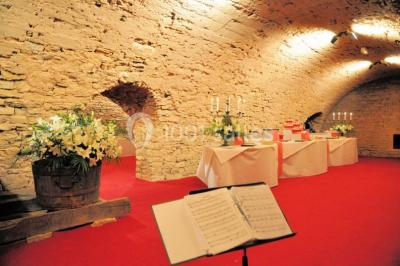 Cour éclairée au crépuscule avec des bâtiments en pierre, des torches allumées et des personnes en arrière-plan.