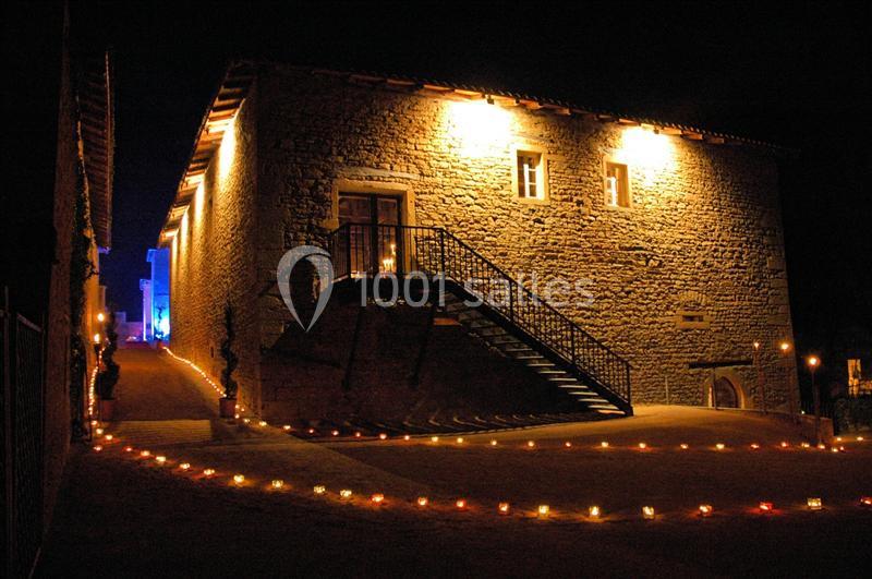 Bâtiment en pierre éclairé la nuit, avec des bougies alignées au sol et un escalier extérieur en métal.