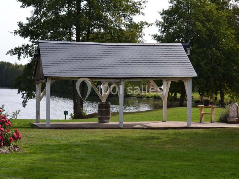 Abri en bois avec toit en ardoise, situé près d'un lac entouré de pelouse et d'arbres.