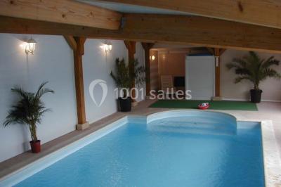 Piscine intérieure avec eau bleue, entourée de plantes en pot et éclairée par des appliques murales.