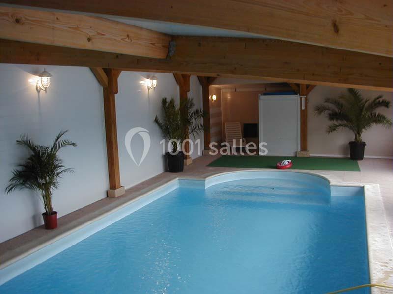 Piscine intérieure avec eau bleue, entourée de plantes en pot et éclairée par des appliques murales.