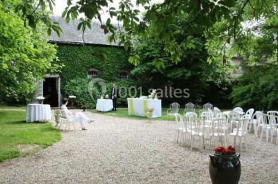 Salle de réception lumineuse avec tables rondes dressées, chaises blanches et décorations florales élégantes.