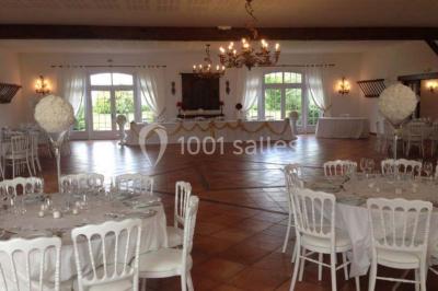 Salle de réception lumineuse avec tables rondes dressées, chaises blanches et décorations florales élégantes.