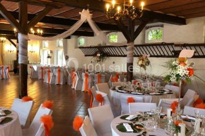 Salle de réception lumineuse avec tables rondes dressées, chaises blanches et décorations florales élégantes.