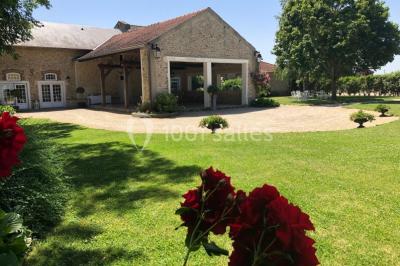 Salle de réception lumineuse avec tables rondes dressées, chaises blanches et décorations florales élégantes.