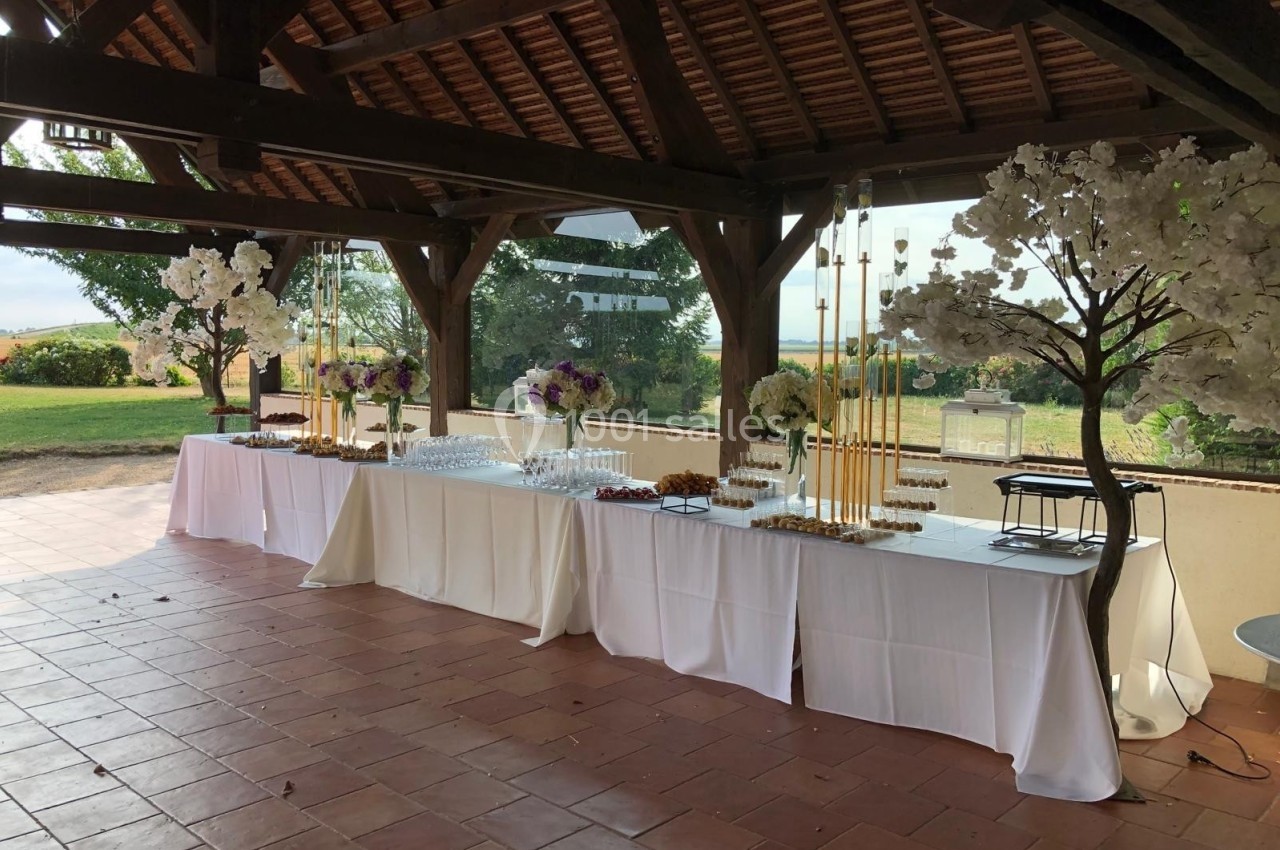 Table de buffet dressée sous une pergola en bois, décorée de fleurs blanches et offrant une vue sur un jardin.