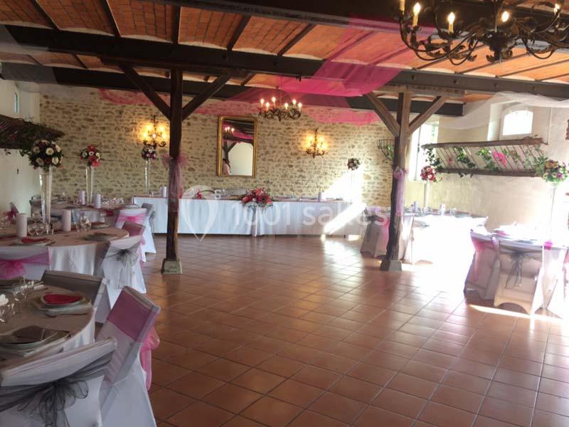 Salle de réception décorée avec des nappes blanches, des chaises ornées de rubans roses et des arrangements floraux.