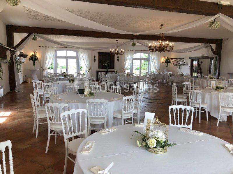 Salle de réception décorée avec des tables rondes, nappes blanches, chaises assorties et ornements floraux.