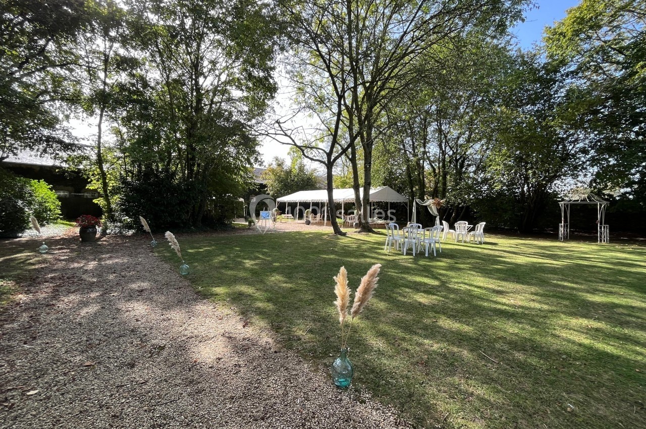 Jardin avec pelouse, chaises blanches, tente blanche et arbres, décoré pour un événement en plein air.