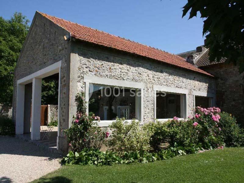 Bâtiment en pierre avec toit en tuiles, grandes fenêtres et jardin fleuri au premier plan.