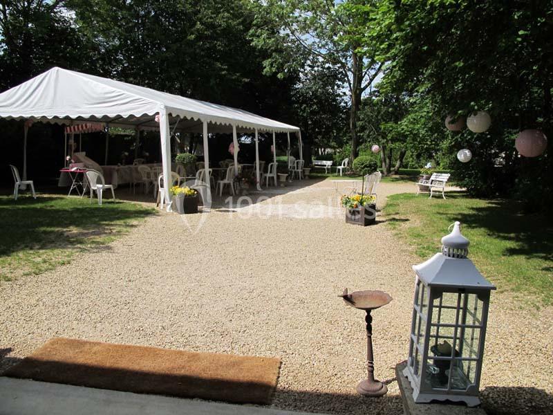 Tente blanche installée sur un espace extérieur gravillonné, entourée de verdure et décorée de lanternes et fleurs.