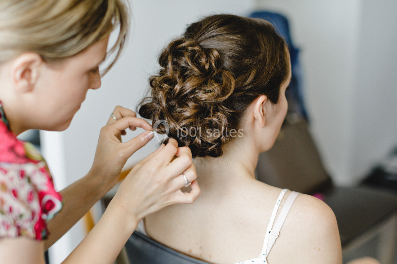 Une coiffeuse attache les cheveux d'une femme en un chignon élaboré dans un cadre intérieur.