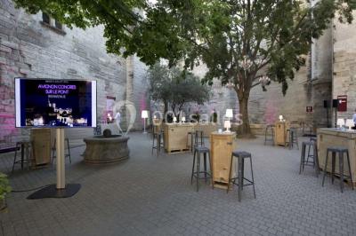 Façade vitrée d'un bâtiment moderne avec éclairages rouges, intégrée à des murs en pierre ancienne.