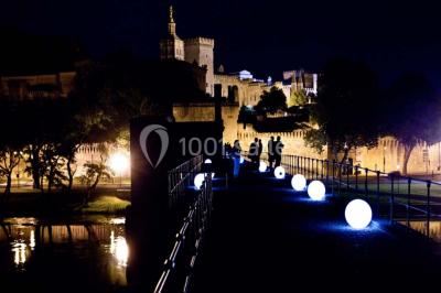 Façade vitrée d'un bâtiment moderne avec éclairages rouges, intégrée à des murs en pierre ancienne.